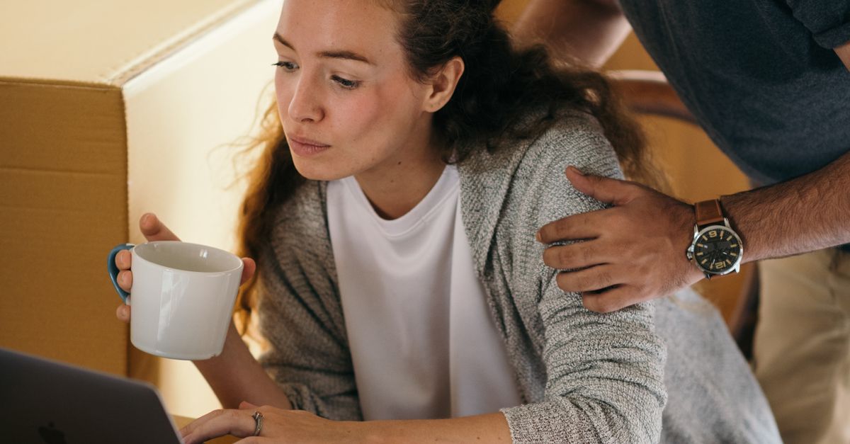 Couple using a laptop beside packed boxes, representing practical planning and important deadlines during a family transition.