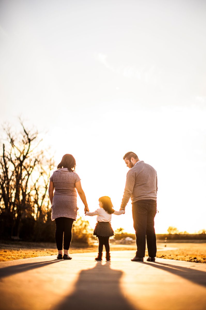 Parents holding hands with their child outdoors at sunset